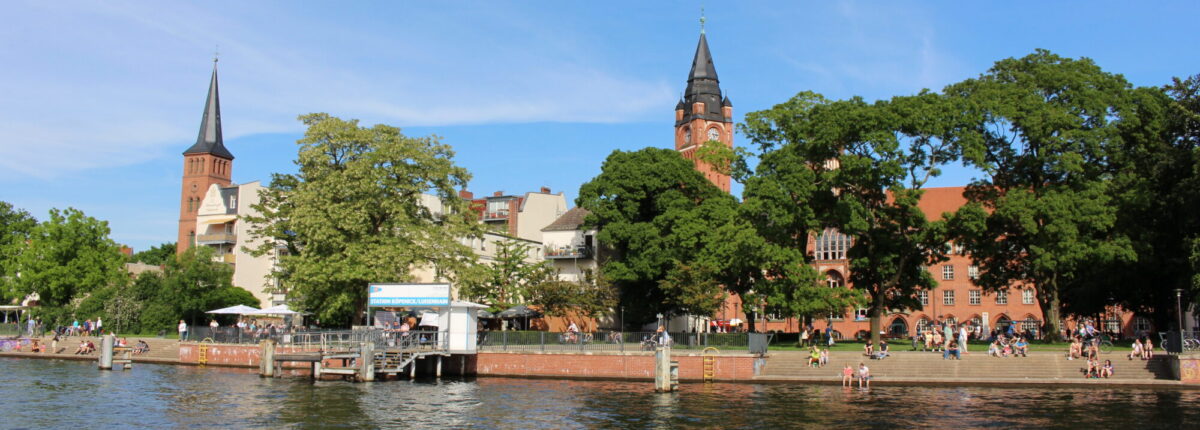 Der Luisenhain im Sommer, während das historische Rathaus Köpenick und die Stadtkirche Köpenick im Hintergrund majestätisch über der Spree thronen