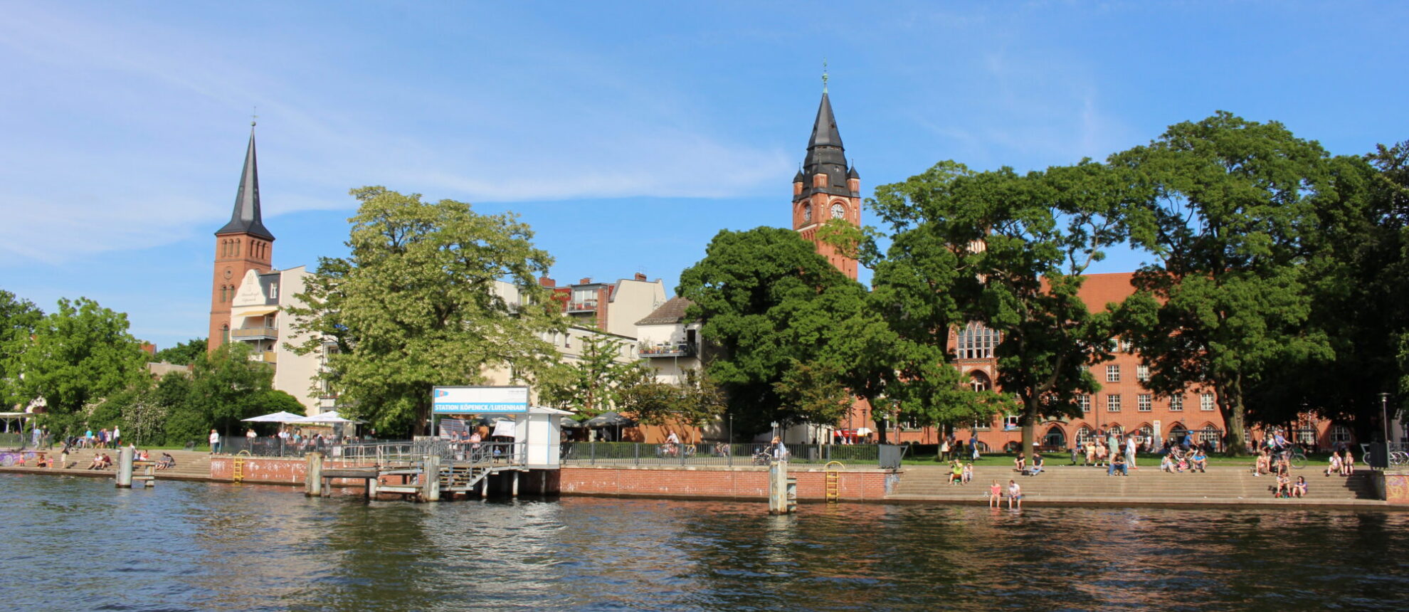 Der Luisenhain im Sommer, während das historische Rathaus Köpenick und die Stadtkirche Köpenick im Hintergrund majestätisch über der Spree thronen